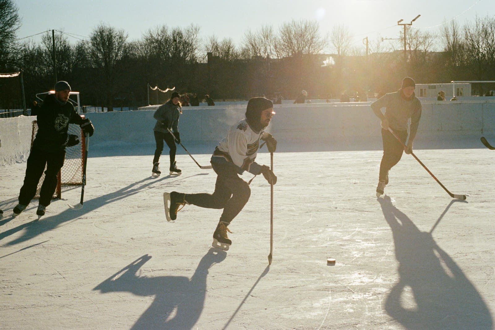 Adults playing shinny on an outdoor community rink in low winter sun