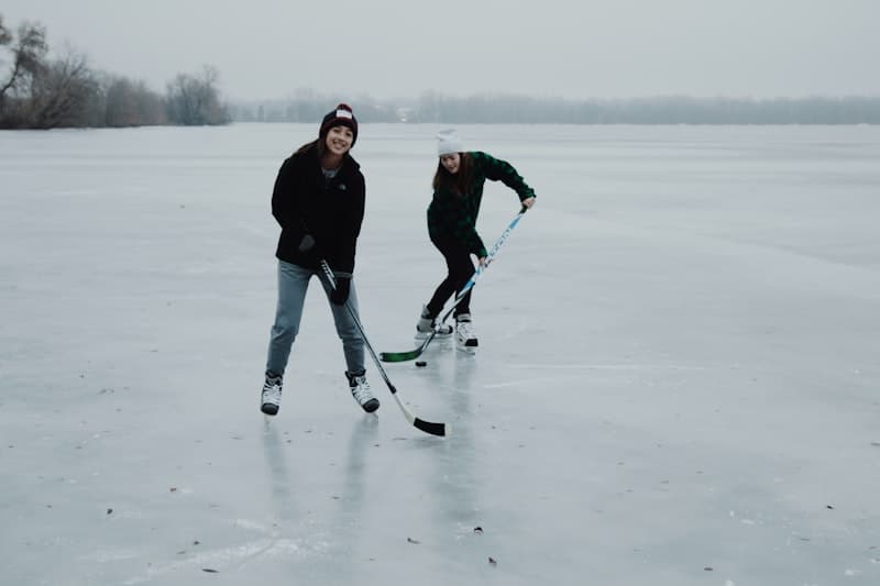 Two women playing shinny on a frozen lake, smiling